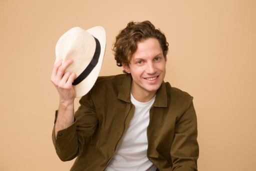 homme portant une chemise marron tenant un chapeau fedora blanc
